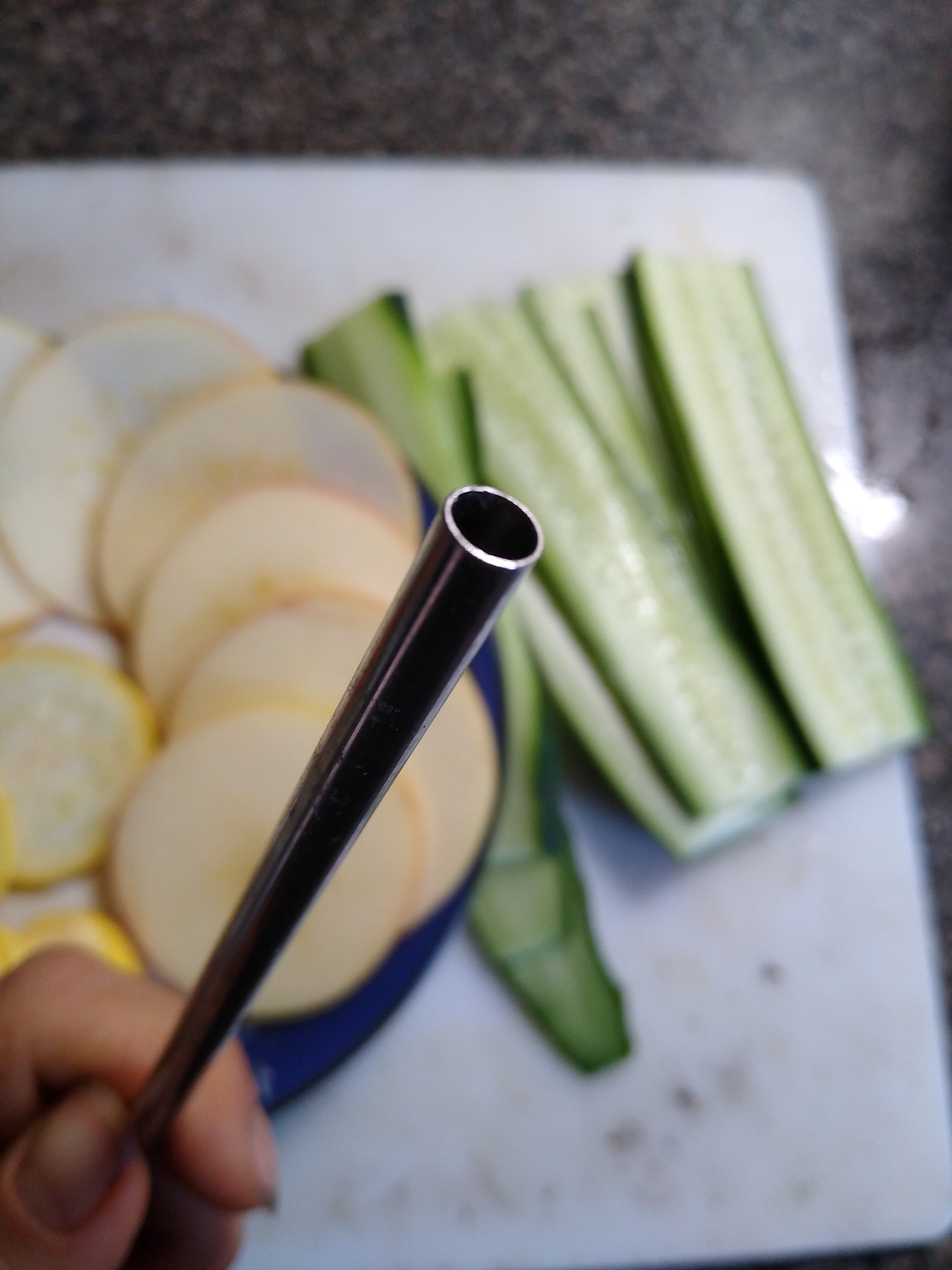 Close up of end of stainless steel straw. In background, cucumber and apple slices.
