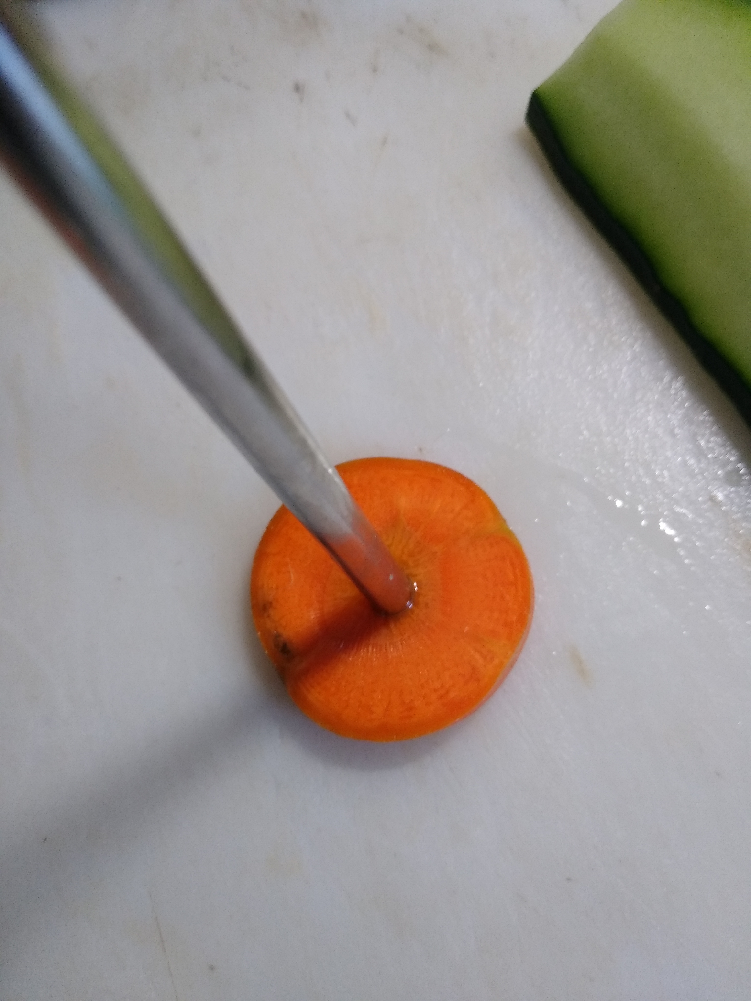 Close up of stainless steel straw punching hole in center of carrot slice.