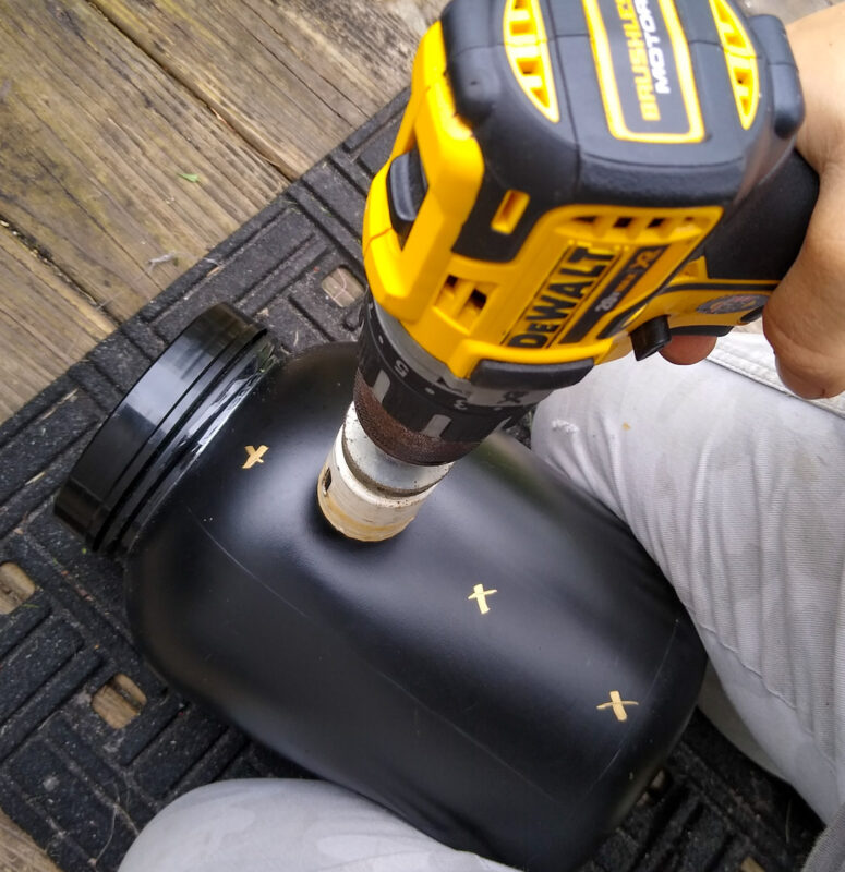 Making DIY hay ball for horses by cutting holes in black food canister with yellow drill. 