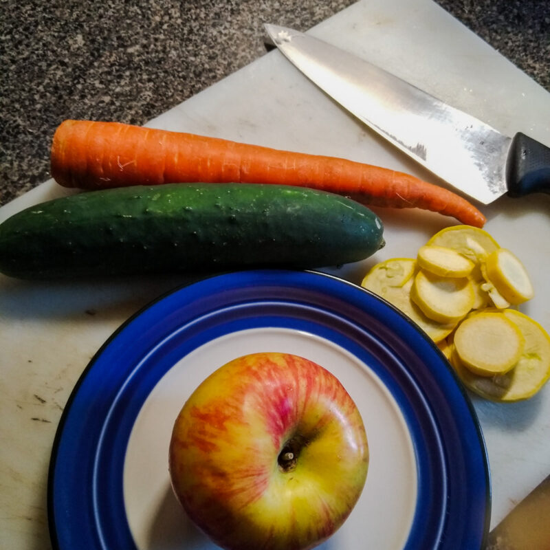 Chef's knife and cutting board with carrot, cucumber, apple, and squash