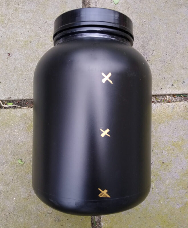 Large black food canister with small X marks in gold marker. 
