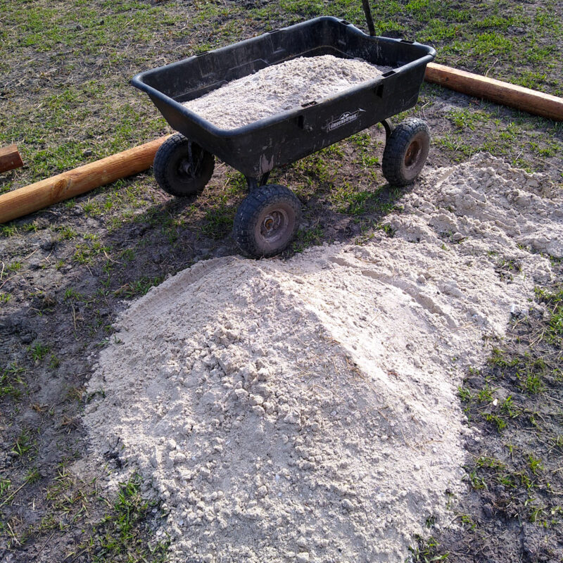 A pile of sand on the ground next to a black wheeled cart full of sand.