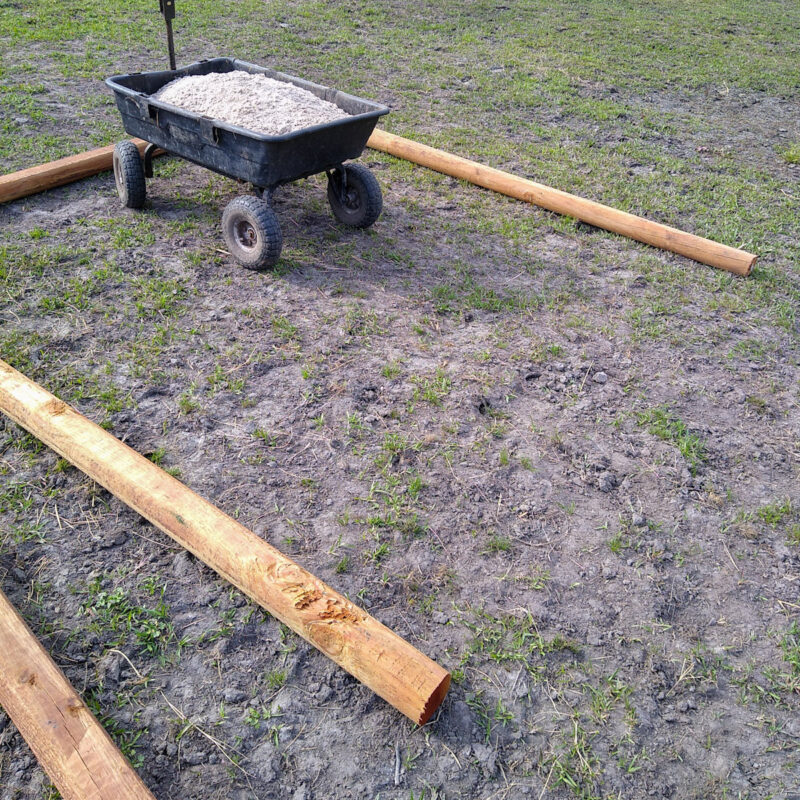 Three timbers forming an open square with a black wheeled cart full of sand in middle.