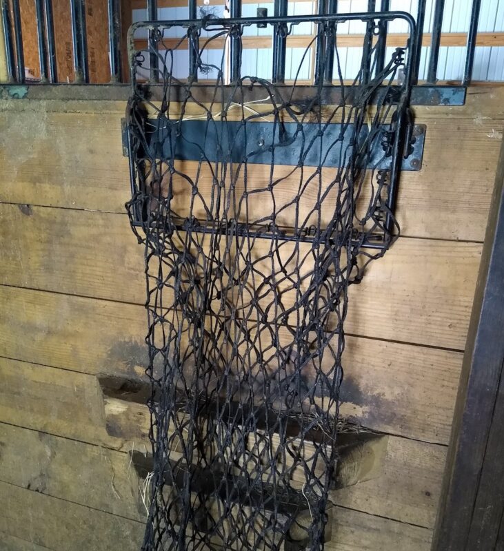 An empty hay net in a metal bracket on a stall wall.