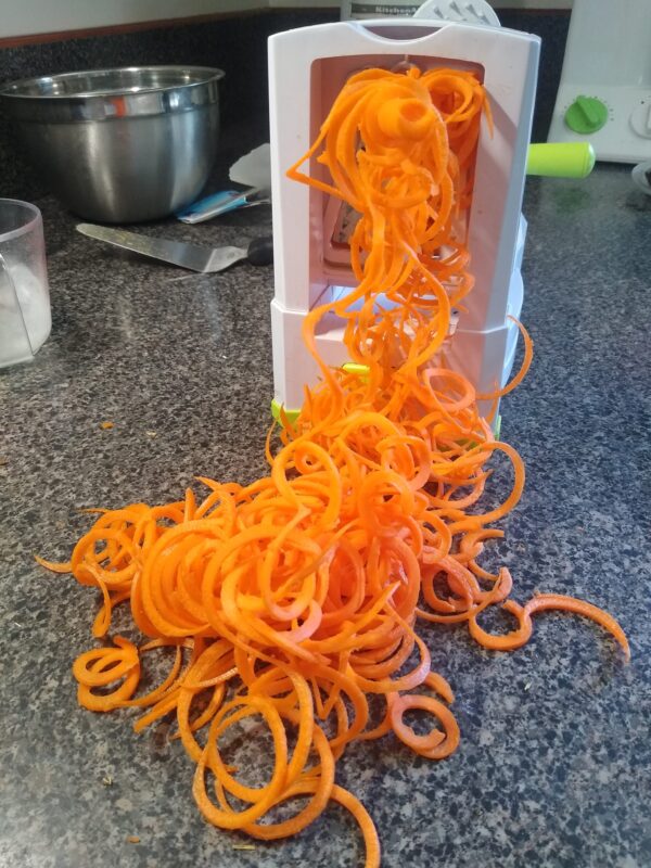 Carrot noodles emerge from the spiralizer before going into the mane sensory board.