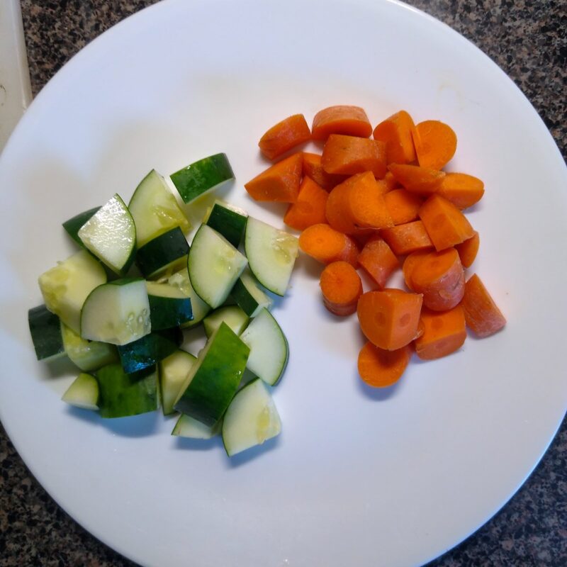 White plate with chopped cucumber and carrots.