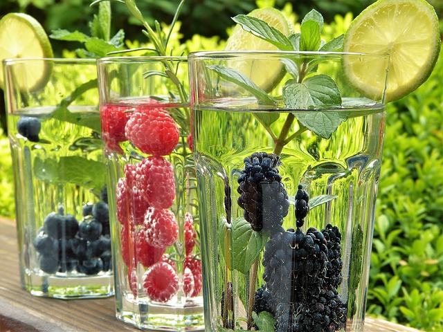 Three glasses of fruit flavored water. From left to right, glass of water with blueberries, raspberries, and blackberries.