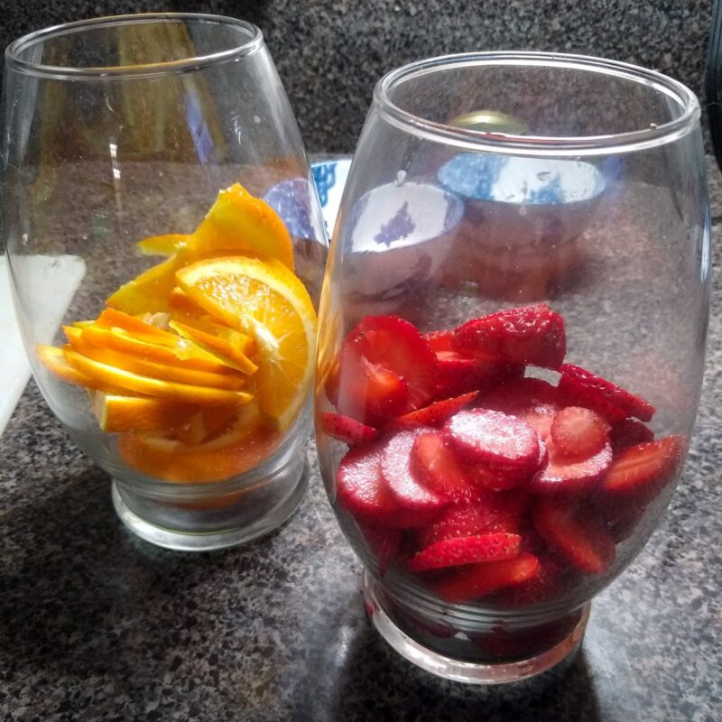 Two glass containers with cut strawberries and sliced oranges. 