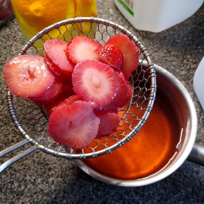 Straining the strawberries out of the finished fruit flavored water for horses.