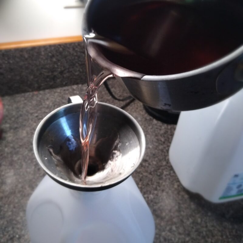 Making fruit flavored water for horses by pouring the strawberry infused water into a jug.