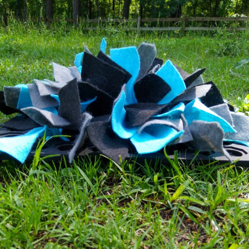 A snuffle mat with black, blue, and gray fabric on a grass background. 