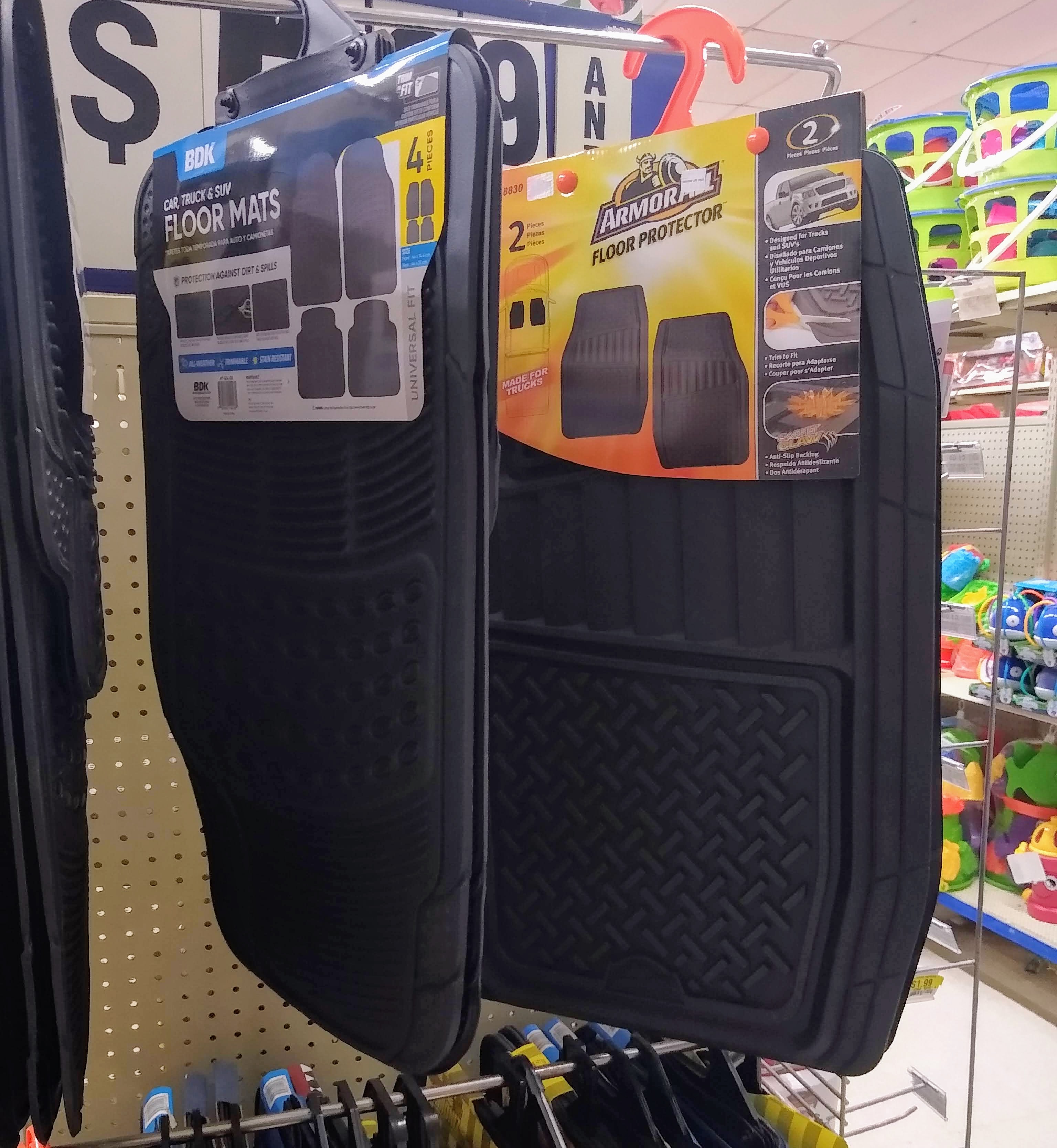 Two sets of black car floor mats hanging on a store display.