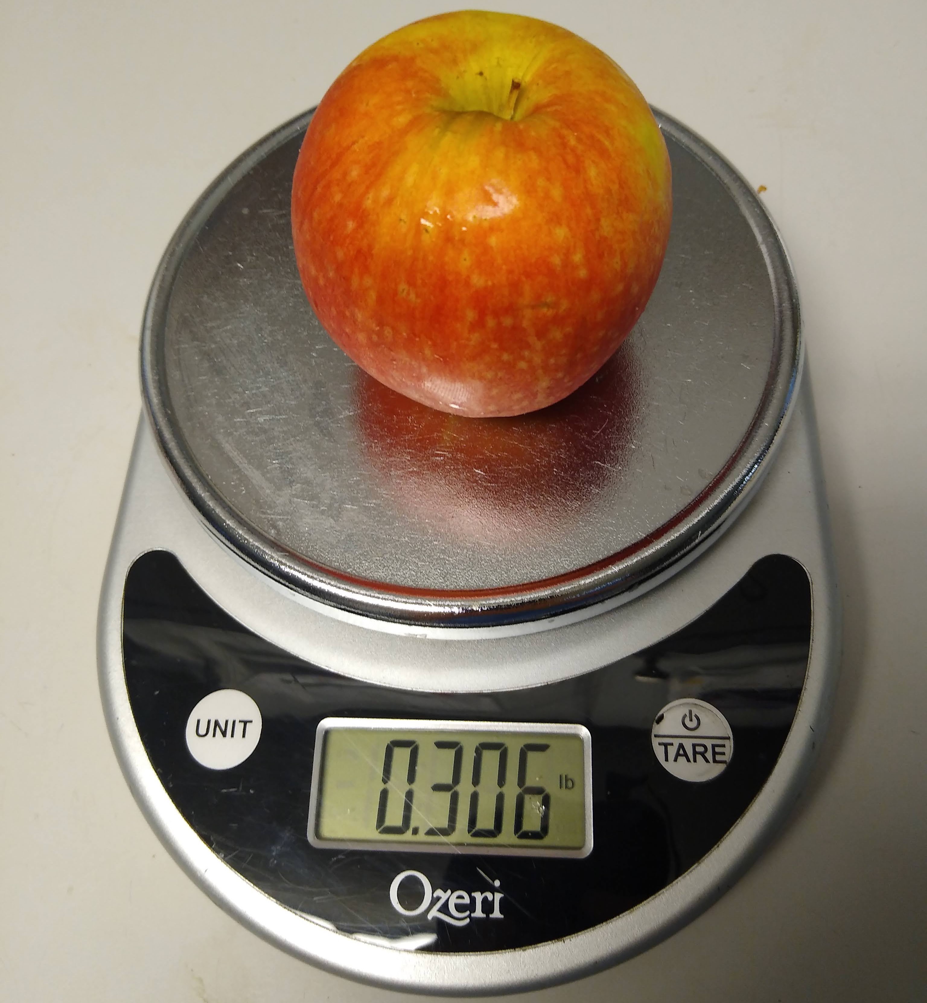 A small silver Ozeri brand scale weighing an apple for a horse. The scale is on and reads 0.306 lb.
