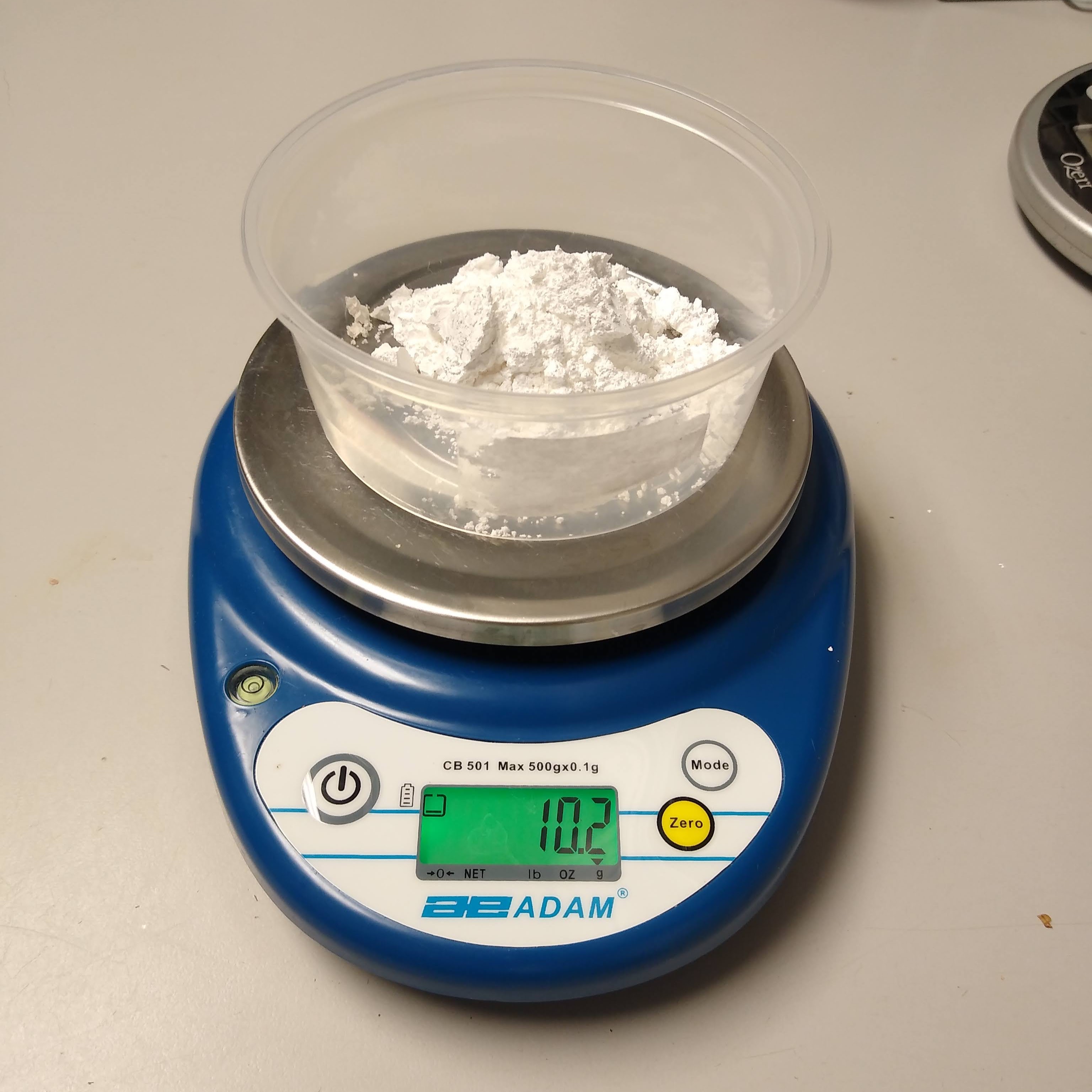 A blue horse feed and supplement scale weighing a white powder in a plastic cup.