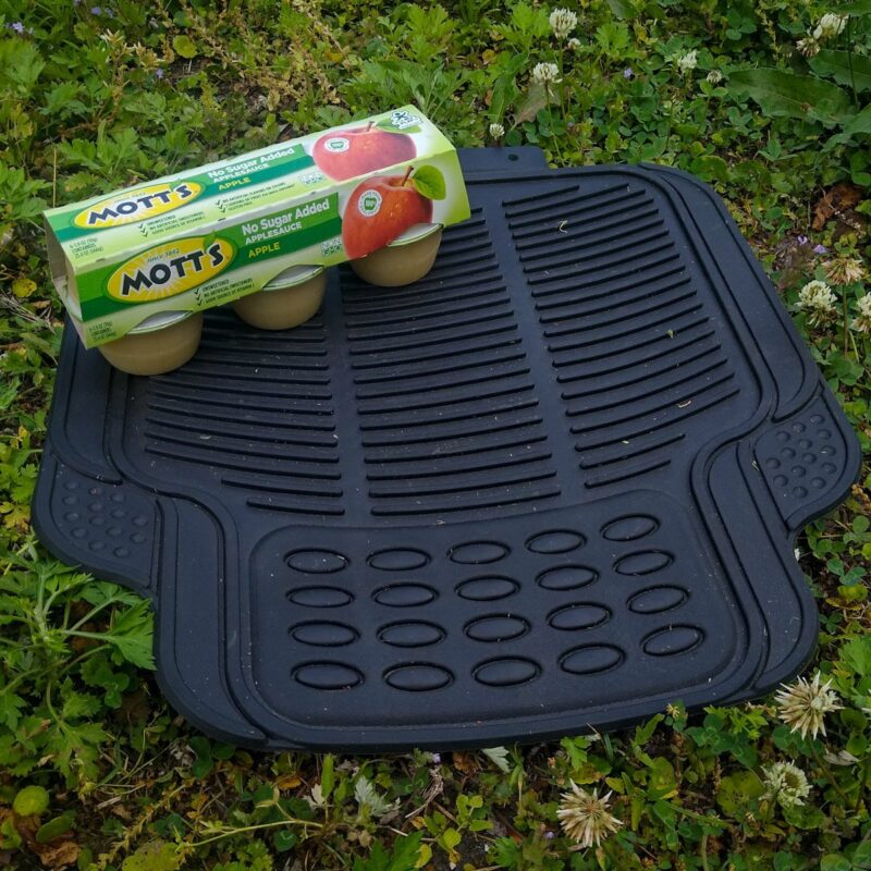 A car's floor mat and pack of applesauce ready to become a DIY horse slow feeder.
