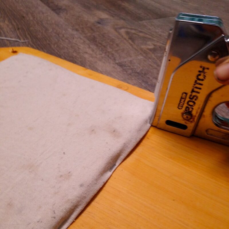 A staple gun applies staples to a piece of canvas on the textured enrichment board.