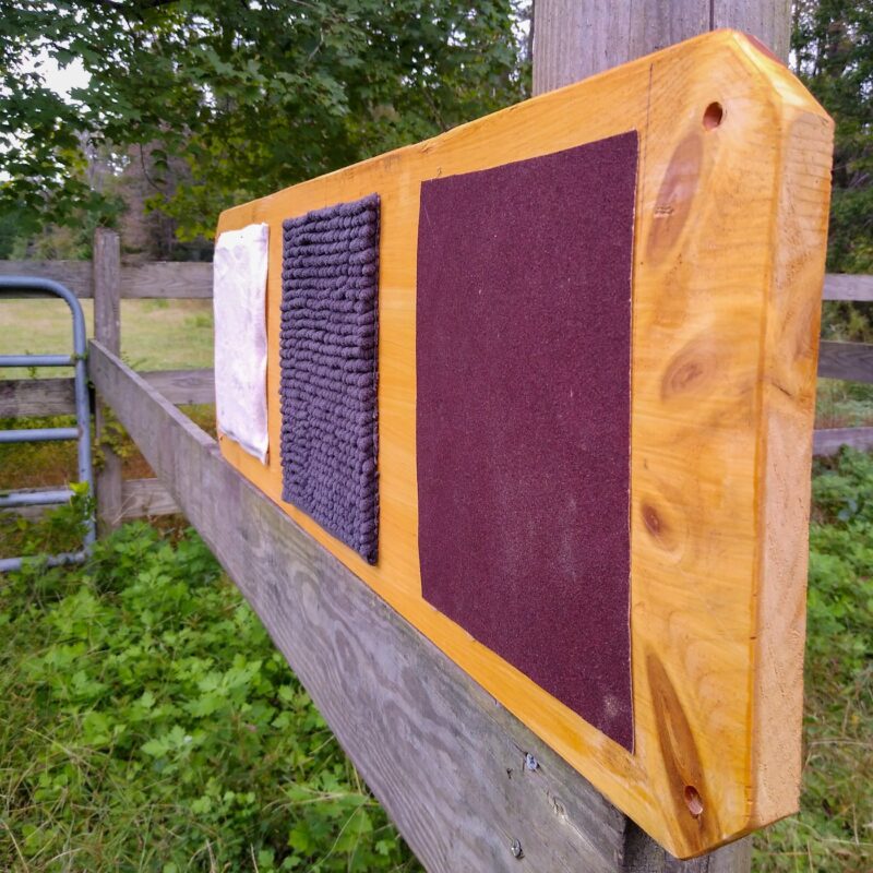 A horse sensory enrichment board for stall enrichment made of a wooden board with textured fabric squares.