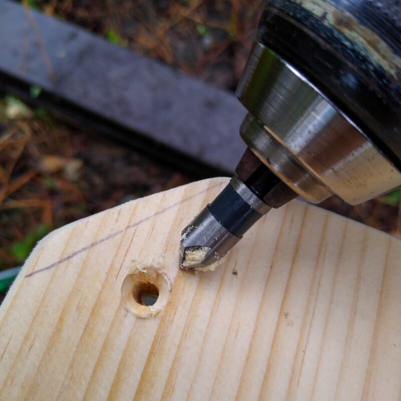 A close up of countersink bit in drill and countersink hole in wooden board.