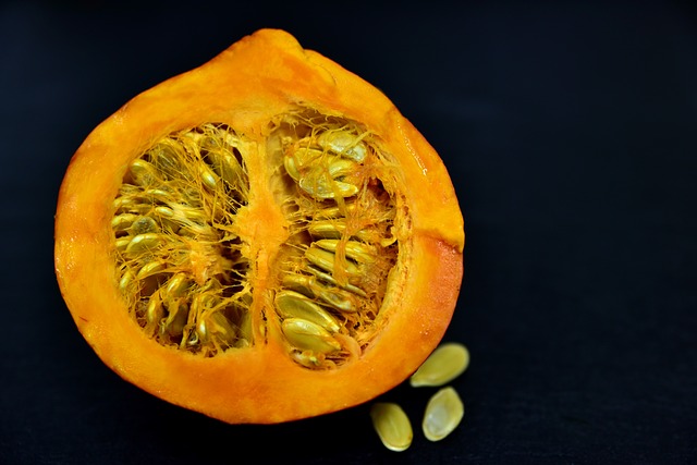 A small pumpkin cut in half and full of seeds on a black background.