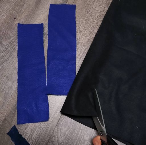 Strips of blue felt fabric for the horse snuffle box. To right, scissors cutting black fabric. 