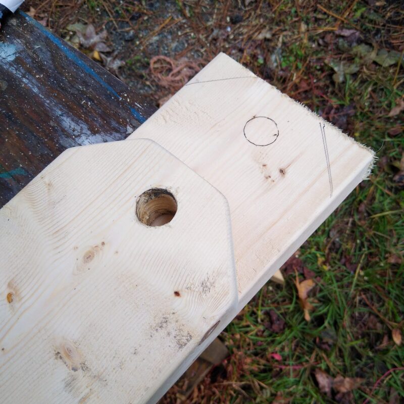 Two pieces of lumber, one cut and with a hole in the center, the other marked for cutting.
