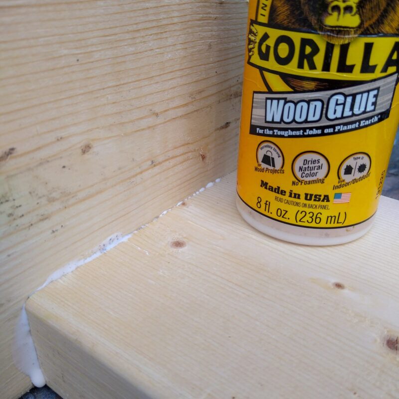 Two pieces of wood joined together with a bead of white wood glue where the pieces meet. A bottle of Gorilla brand wood glue rests on top of the piece of wood.