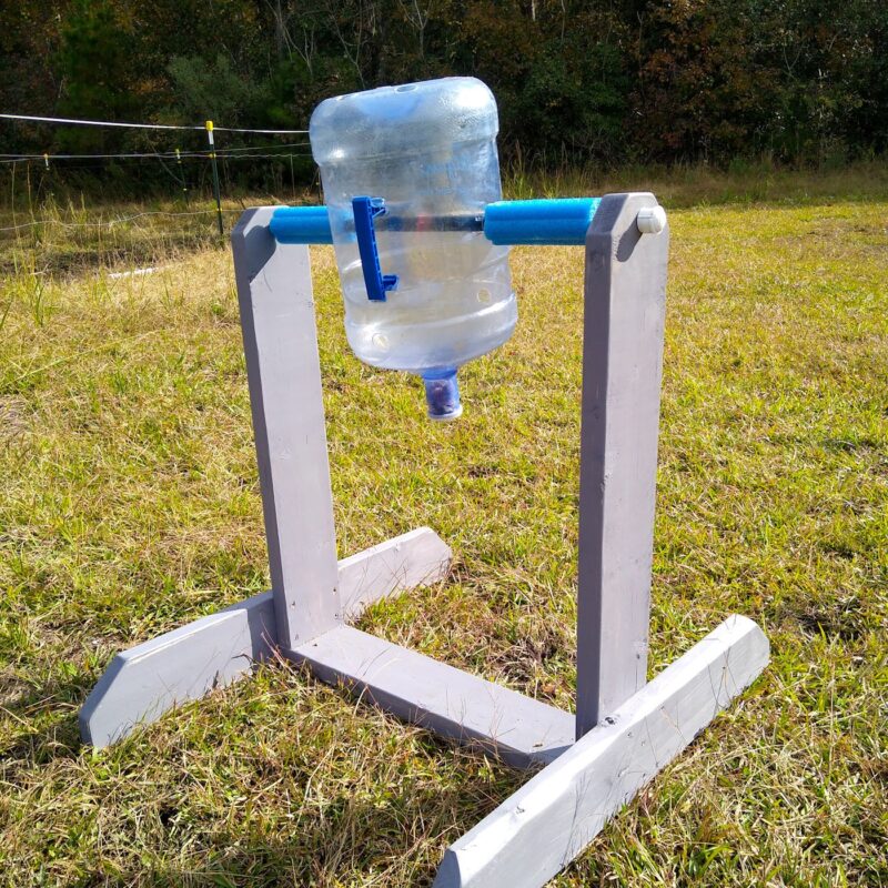 The spin the bottle horse enrichment toy in grass with one blue bottle attached.