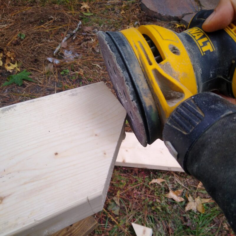 A yellow and black Dewalt orbital sander smoothing down the edges of a piece of lumber.
