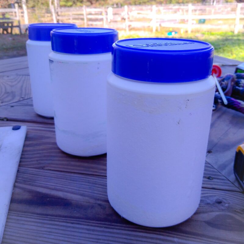 Three white plastic jars with blue lids, one in front of the other.