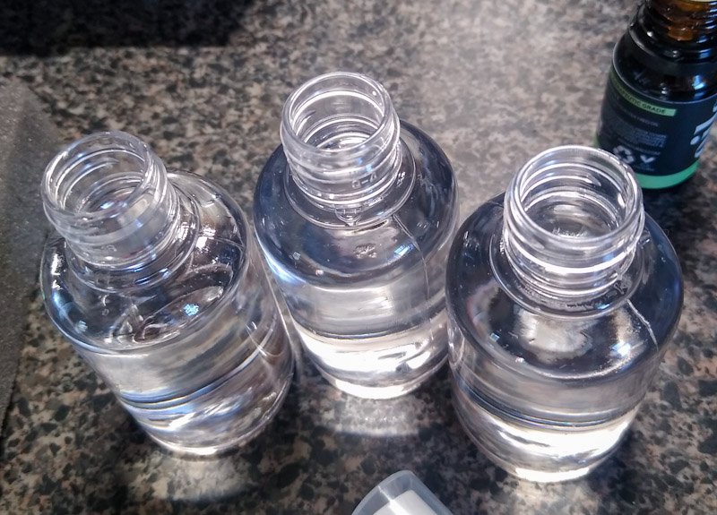 Three spritz bottles or pump sprayers, transparent plastic, filled with clear vodka and seen from above