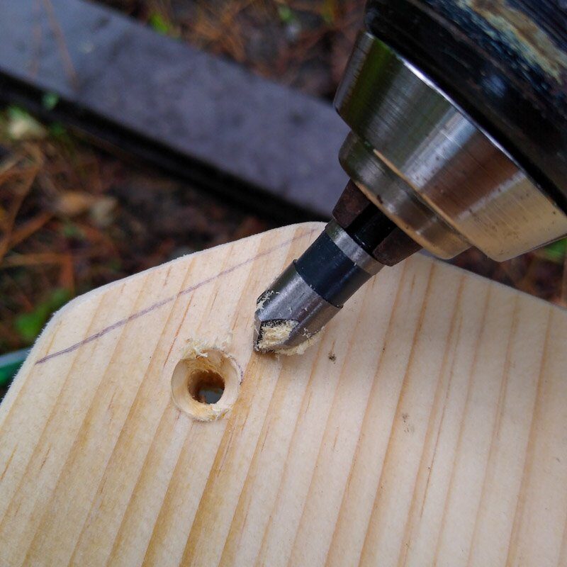 A countersink bit shown next to a close up of a pilot hole in a wooden board.