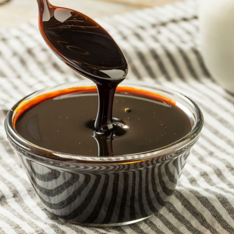 Small glass bowl of molasses with spoon drizzling molasses into bowl