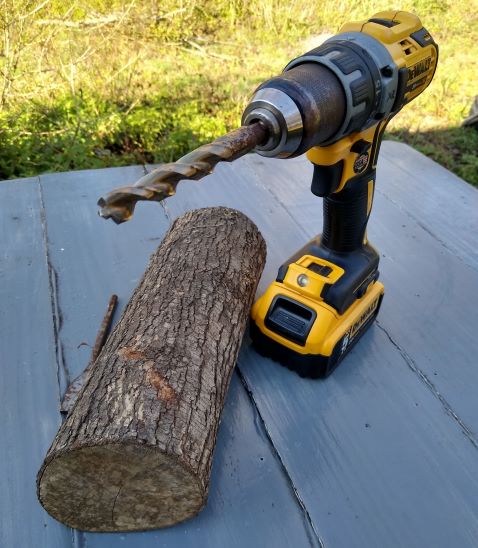 A cordless DeWalt drill with large drill bit and short thick pecan log.
