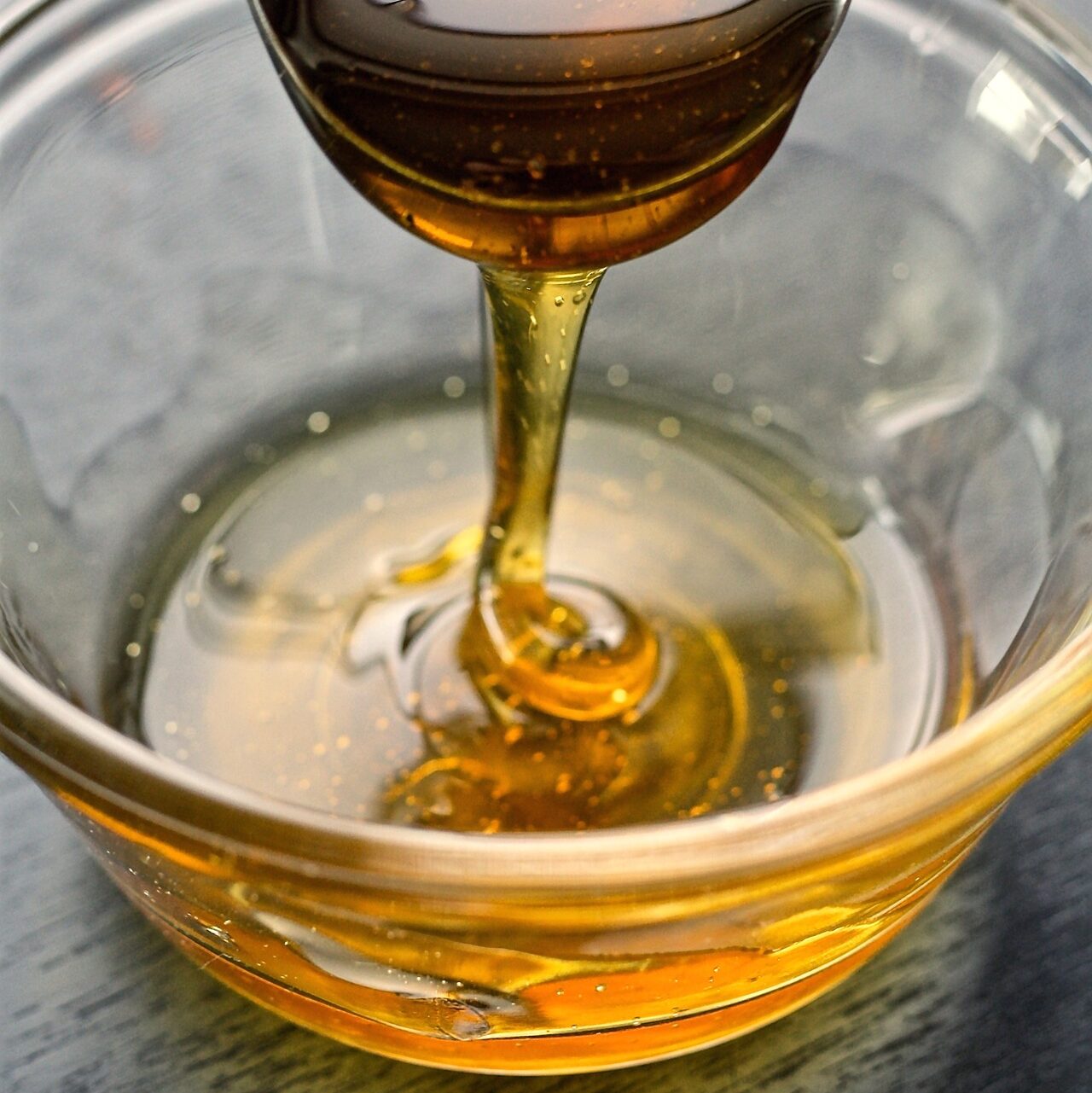 Small glass bowl of honey with spoon drizzling honey into bowl