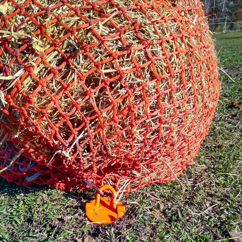 An orange Partrade hay net full of hay clipped to the DIY hay net anchor.