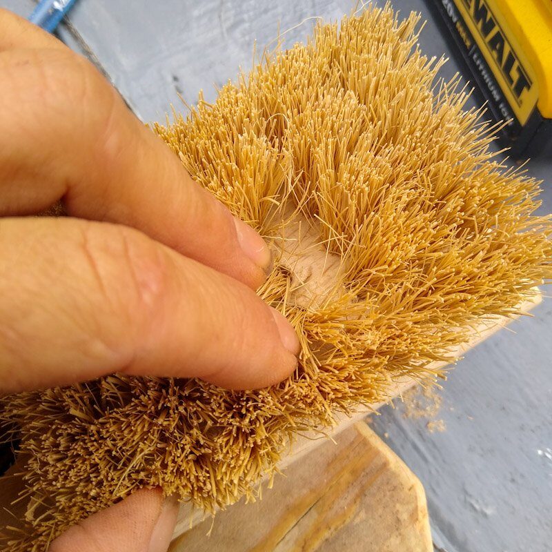 Fingers parting aside scrub brush bristles to show wood underneath