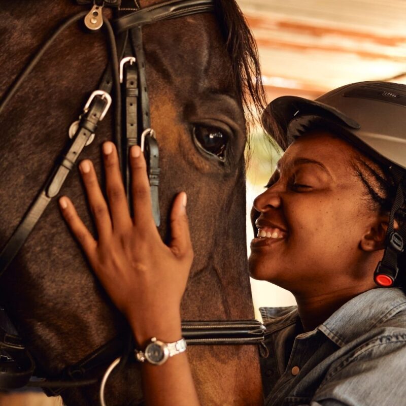 A young Black girl smiles and hugging her horse's face. 