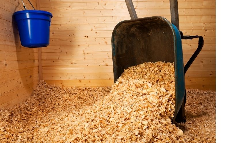 A wheelbarrow full of wood shavings overturned in a horse stall.