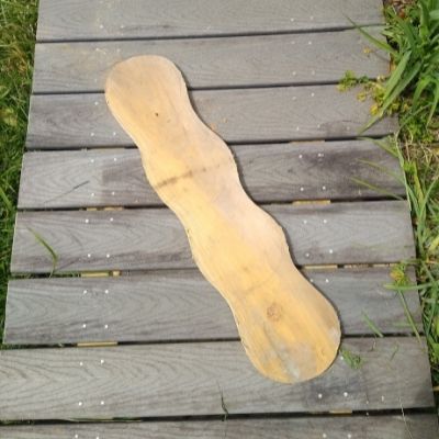A pine board cut into a curvy shape against a wooden walkway.