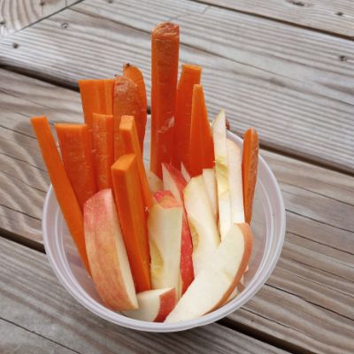 A cup of carrot sticks and apple wedges for horse treats.