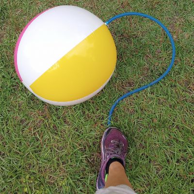 Beach ball inflated against grass background. Human foot in lower edge using yoga ball pump to inflate ball.