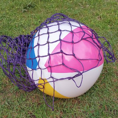 Hay net being wrapped around inflated beach ball to create an easy stable enrichment toy for horses.