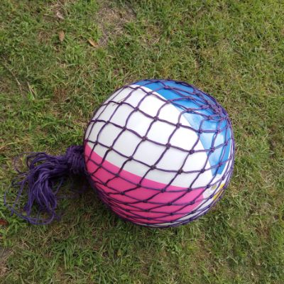 Completed horse treat beach ball hay net toy resting on ground with hay net wrapping around ball and tied at top.