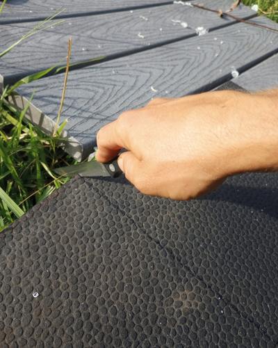 Close up of hand using a serrated steak knife to cut a rubber mat to size