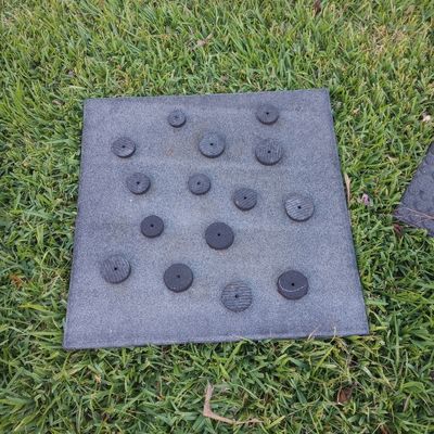 Unfinished horse slow feed mat seen from above on grass background with circular black rubber pieces on top of square rubber base mat.