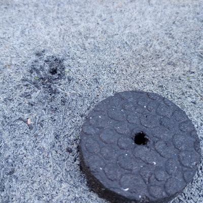 Circular cut piece of rubber on top of plain rubber base mat, each showing one hole from a drill