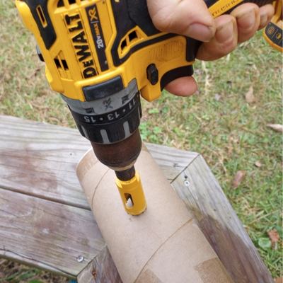 Using a black and yellow DeWalt drill to make a hole in a shipping tube.