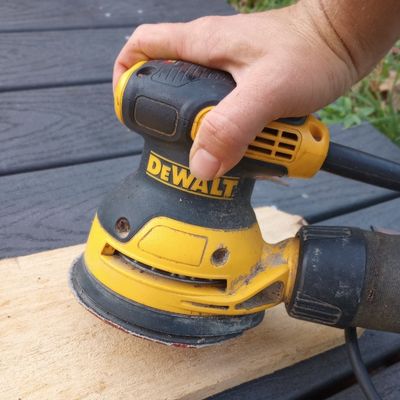 Close up of hand using a DeWalt orbital sander to prepare a scent board for horses.
