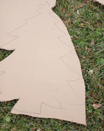 Cutting out the DIY holiday tree for horses by removing excess cardboard, on grass background.