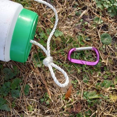Close up of roping coming out of canister feeder toy for horses with purple carabiner on ground beside.